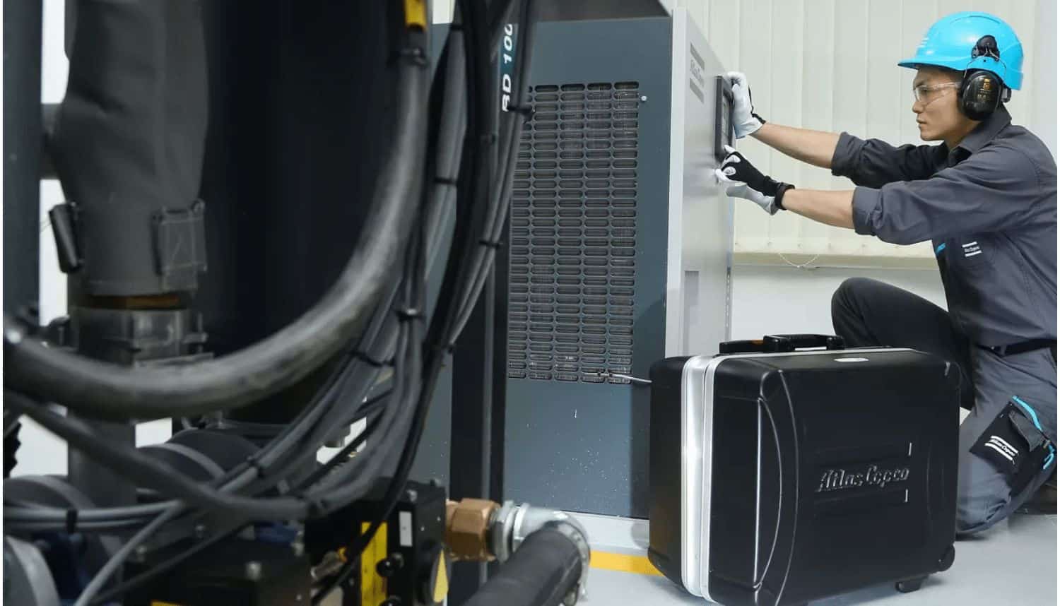 Engineer checking an Atlas Copco air dryer beside compressor pipework