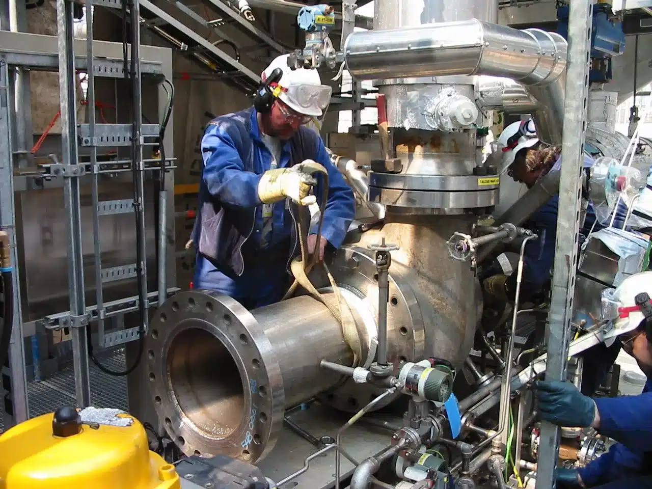 Engineers installing a large flanged valve body on a process skid