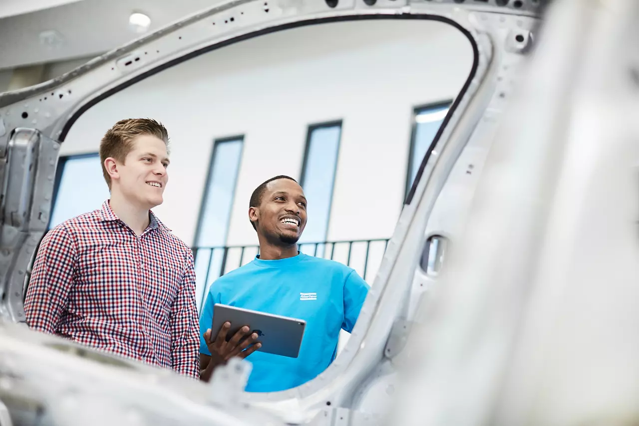 Engineers with a tablet beside a car body shell